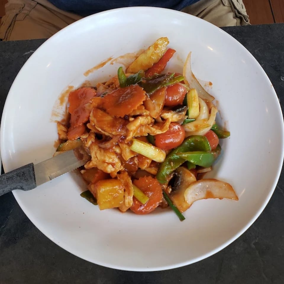 Sweet and sour chicken with bell peppers, carrots, onions, and mushrooms on a white plate.