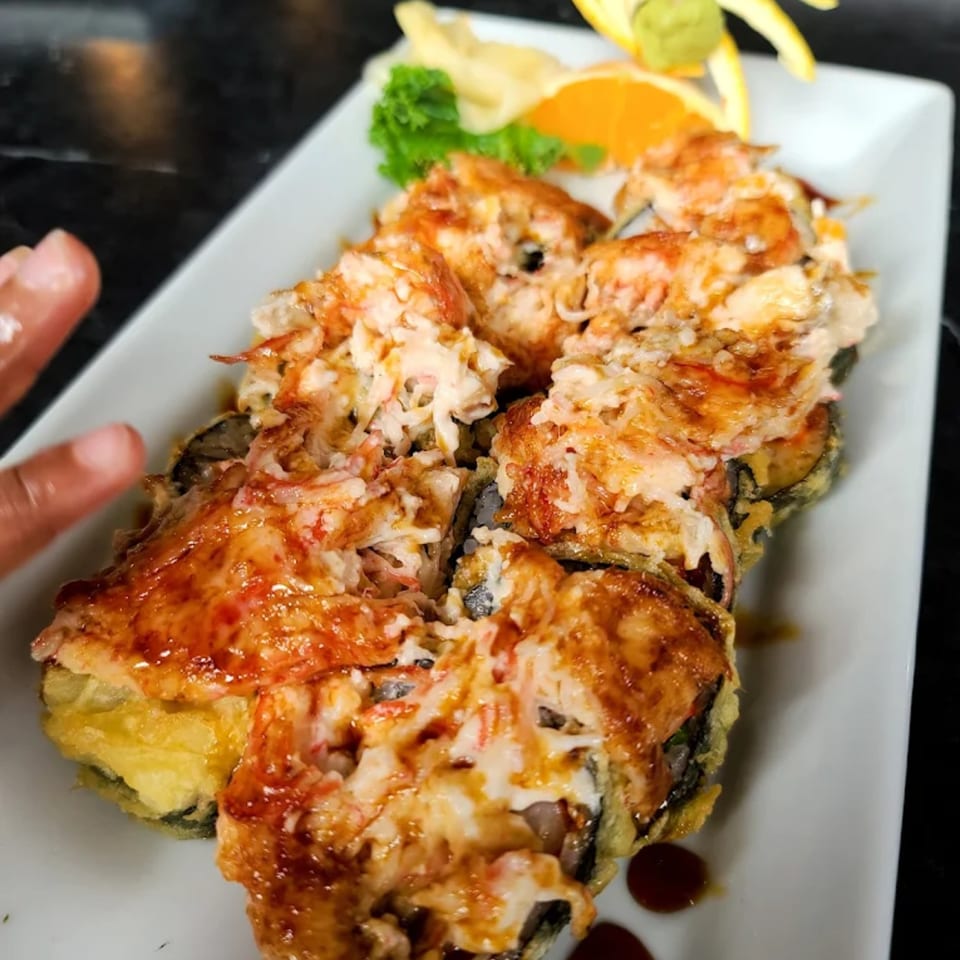A plate of Thai Thai Cocoa Village's crispy fried sushi rolls topped with creamy sauce and garnish.