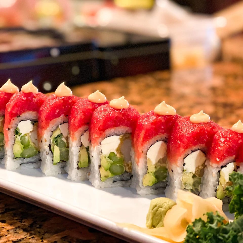 A plate of red-topped sushi rolls with avocado and cream cheese, garnished with wasabi and ginger.