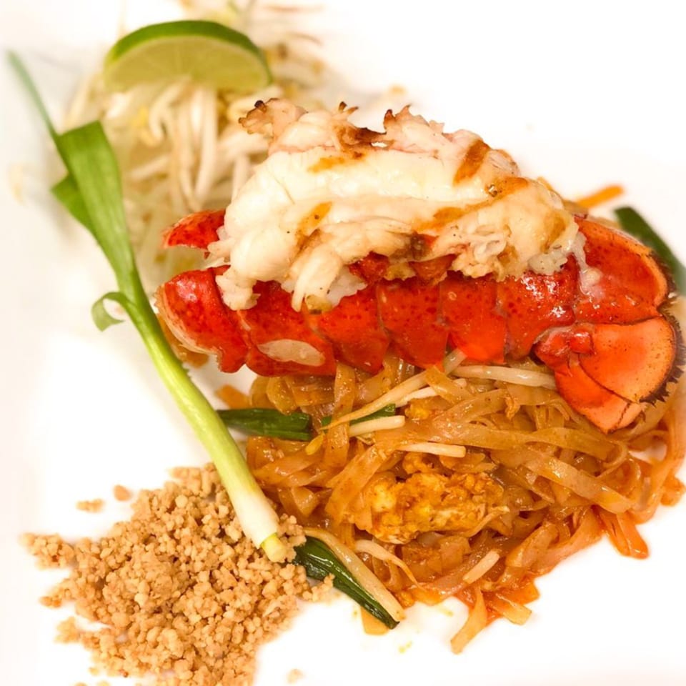Lobster tail Pad Thai with bean sprouts, lime, and crushed peanuts on a white plate.