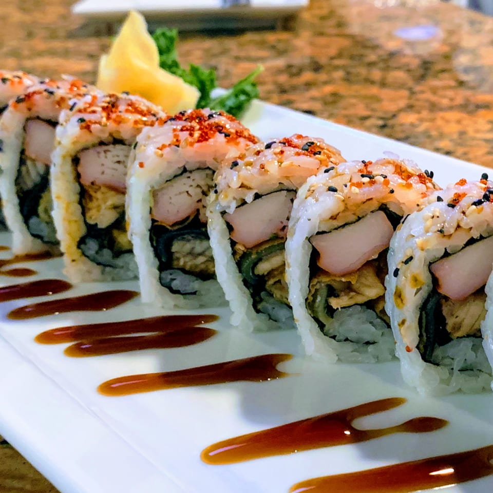 A plate of Thai Thai Cocoa Village sushi rolls with sauce, ginger, and greens.